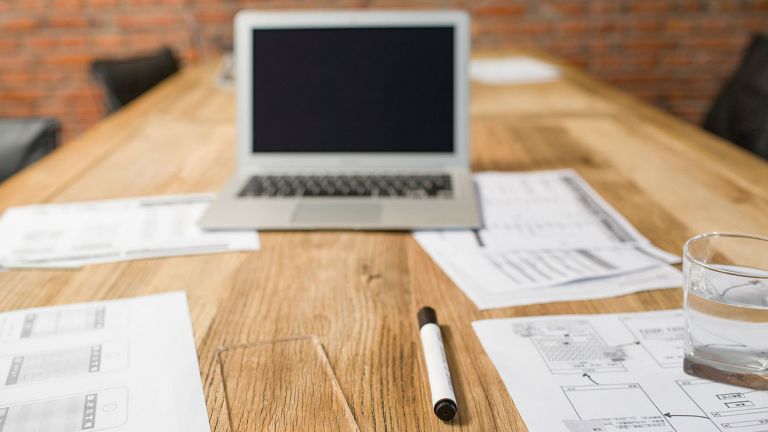 A desk with a laptop, pens and papers.