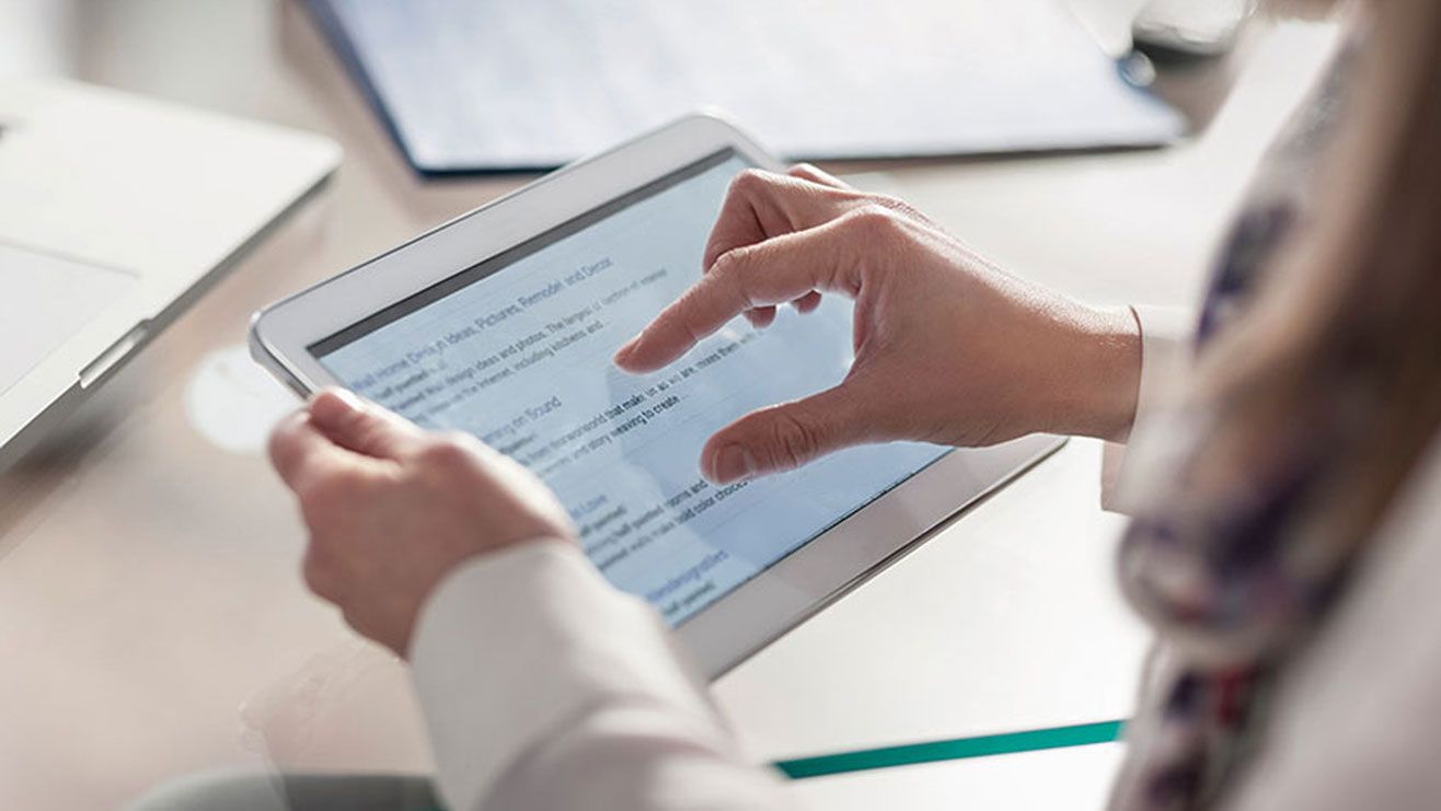 A person reads some text on a tablet using their fingers to scroll down the page