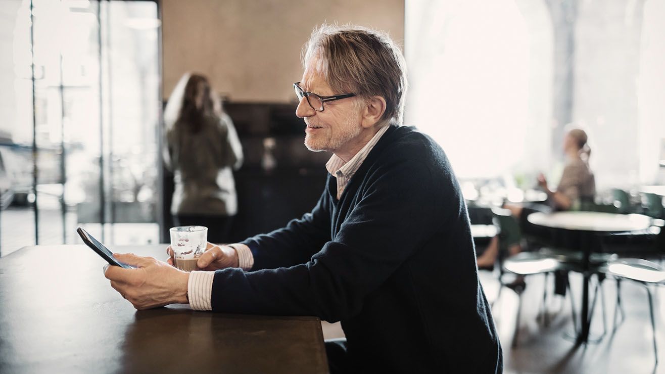  A man sitting at a table in a coffee shop reads his smart phone