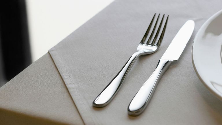  A knife and fork, and a side plate on top of a pale grey napkin