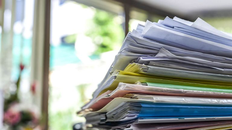  A stack of different coloured cardboard folders filled with paper files