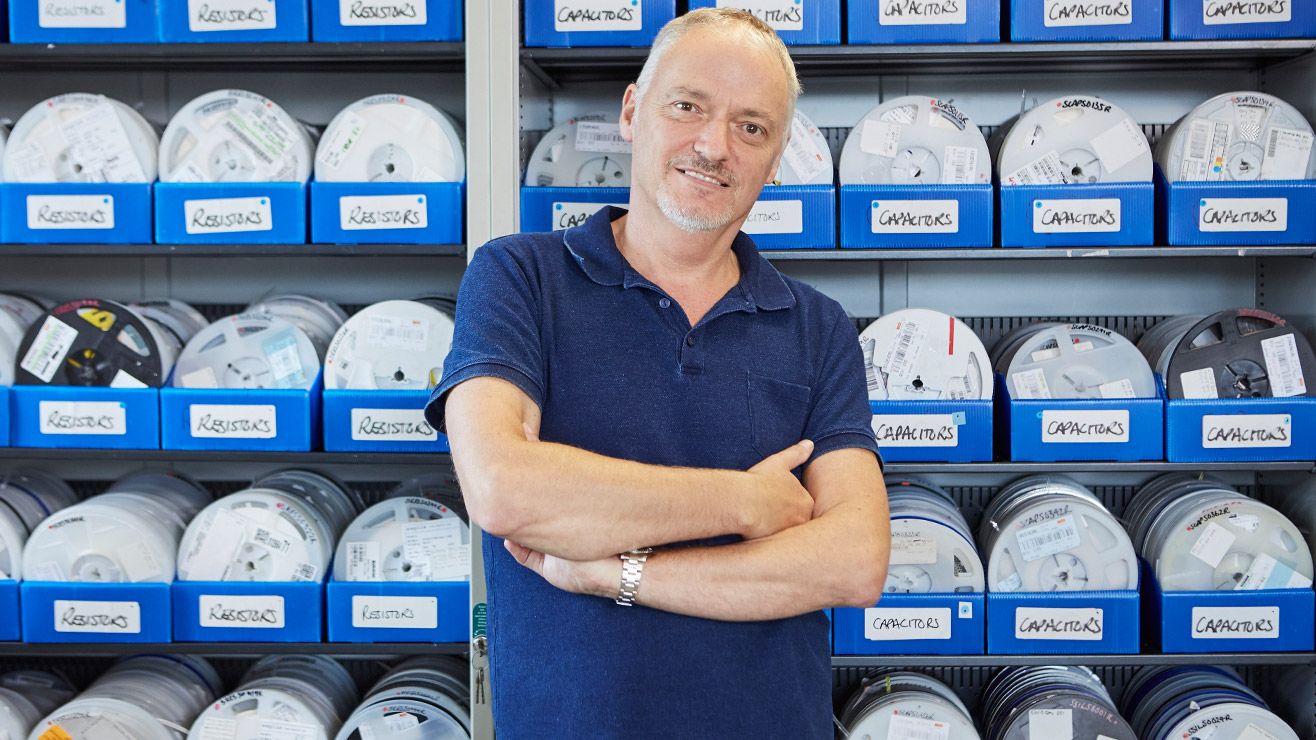 A man standing in front of shelves filled with boxes of wires.