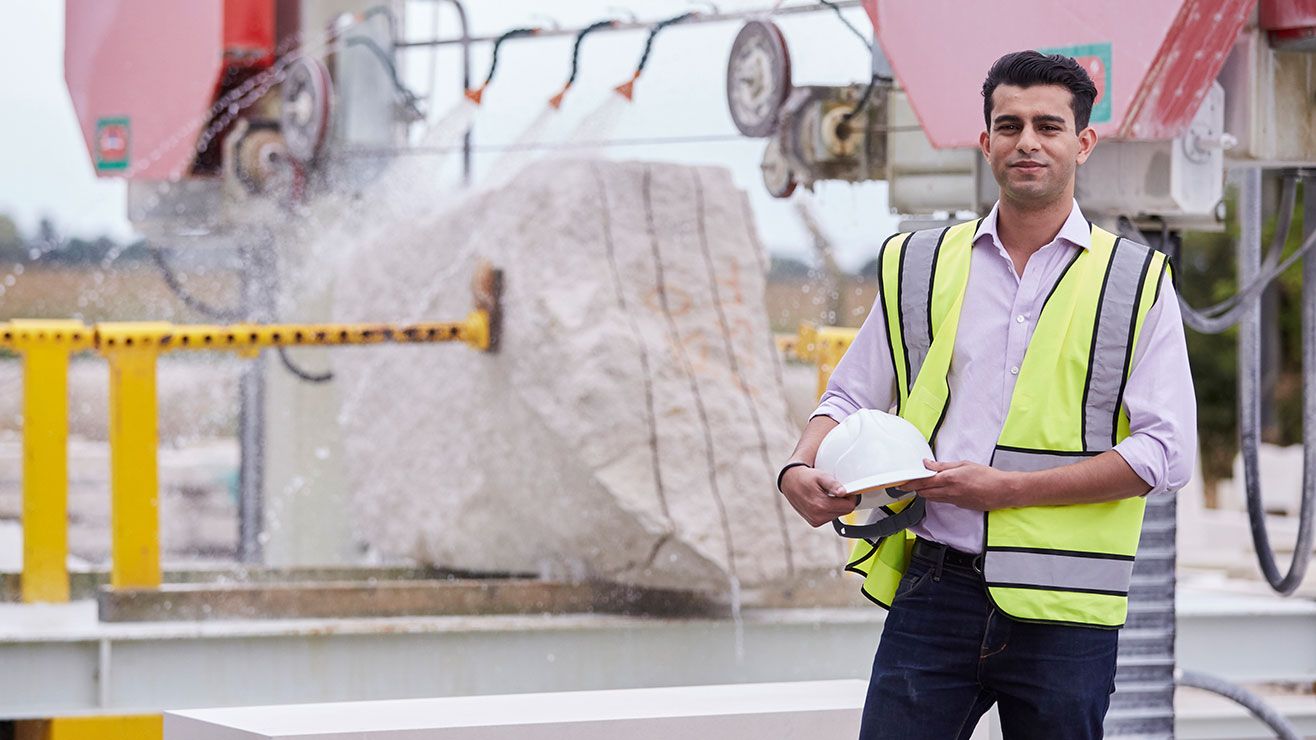 A man on a construction site wearing a high visibilty vest and holding a hard hat.