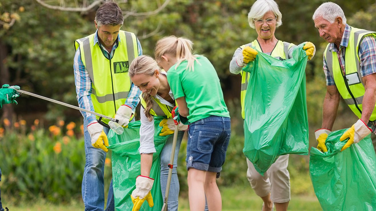  A group of people wearing gardening gloves pick up litter and put it in green bags
