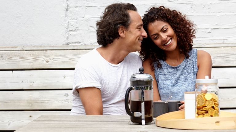 A man and a woman laugh as they sit at a dining table
