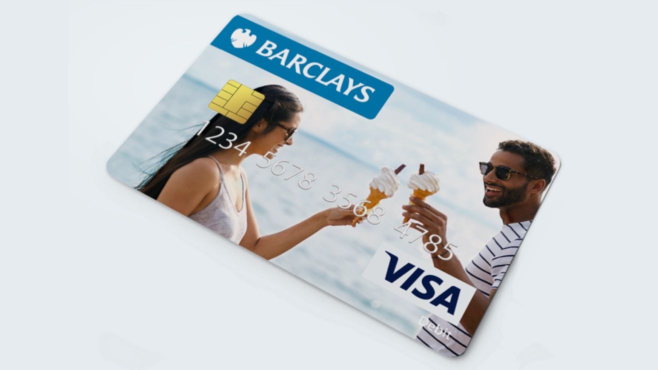 A man holding up a personalised Barclays card in front of a large picture showing the same image
