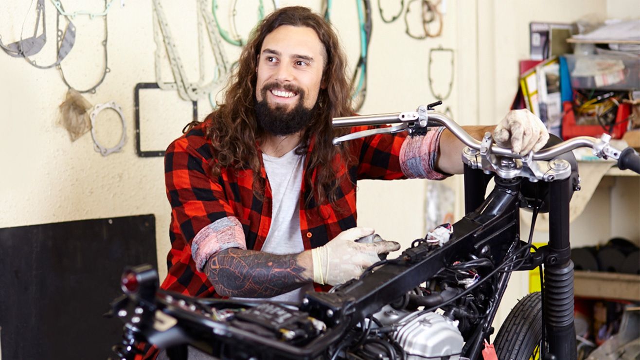 A man wearing protective gloves sits behind a motorbike in a workshop