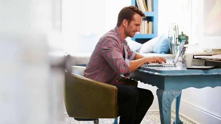 A man working on a latptop at a blue desk at home