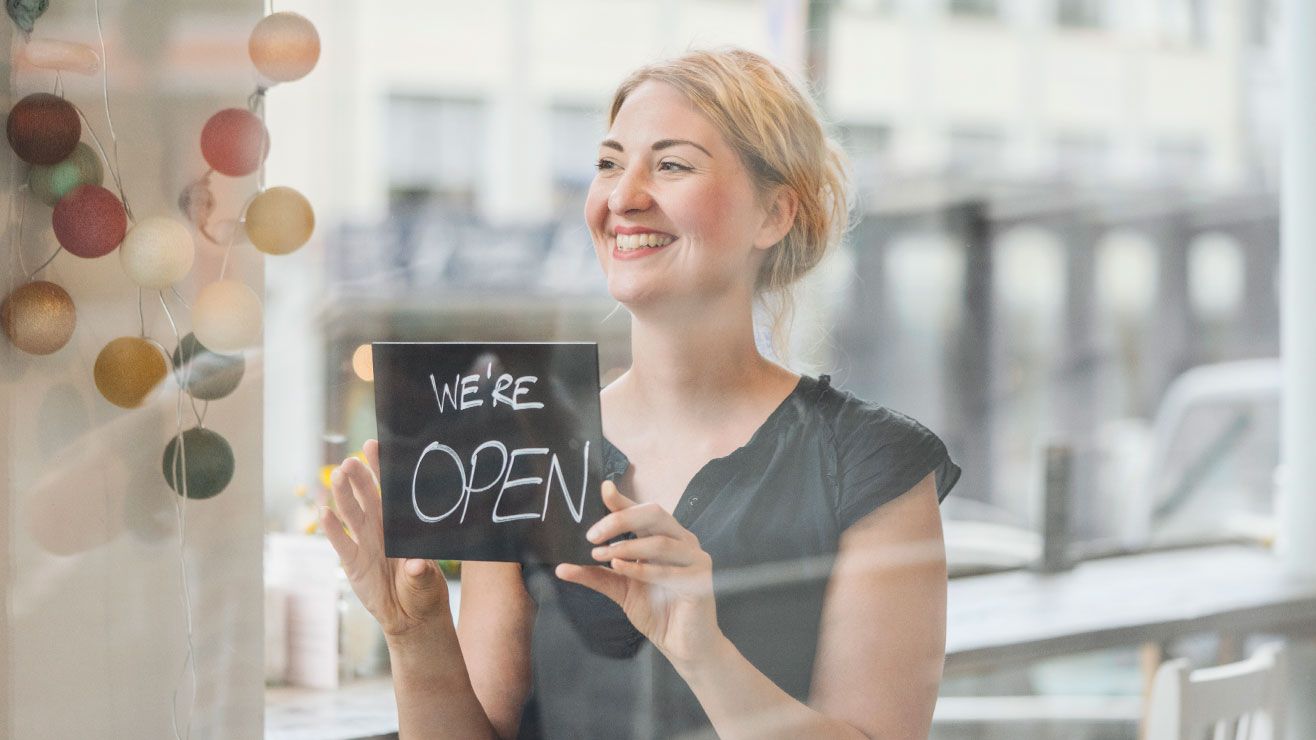 A woman puts up a chalkboard Open sign in the window of a café 
