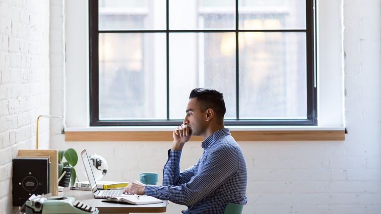 A man looking at a laptop on a desk in a white room