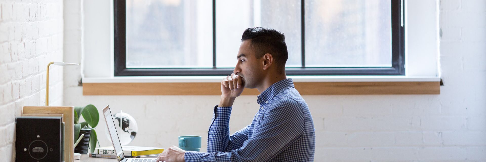 A man looking at a laptop on a desk in a white room