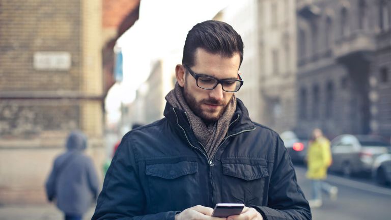  A man standing in a street of a town centre looks at his phone