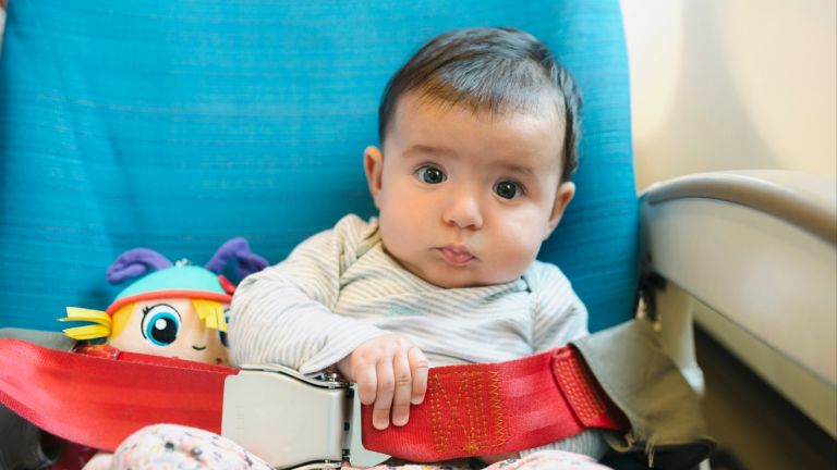 A baby sitting in a plane seat with a cuddly toy beside them