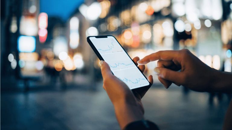 Hands holding a mobile phone in a city at night
